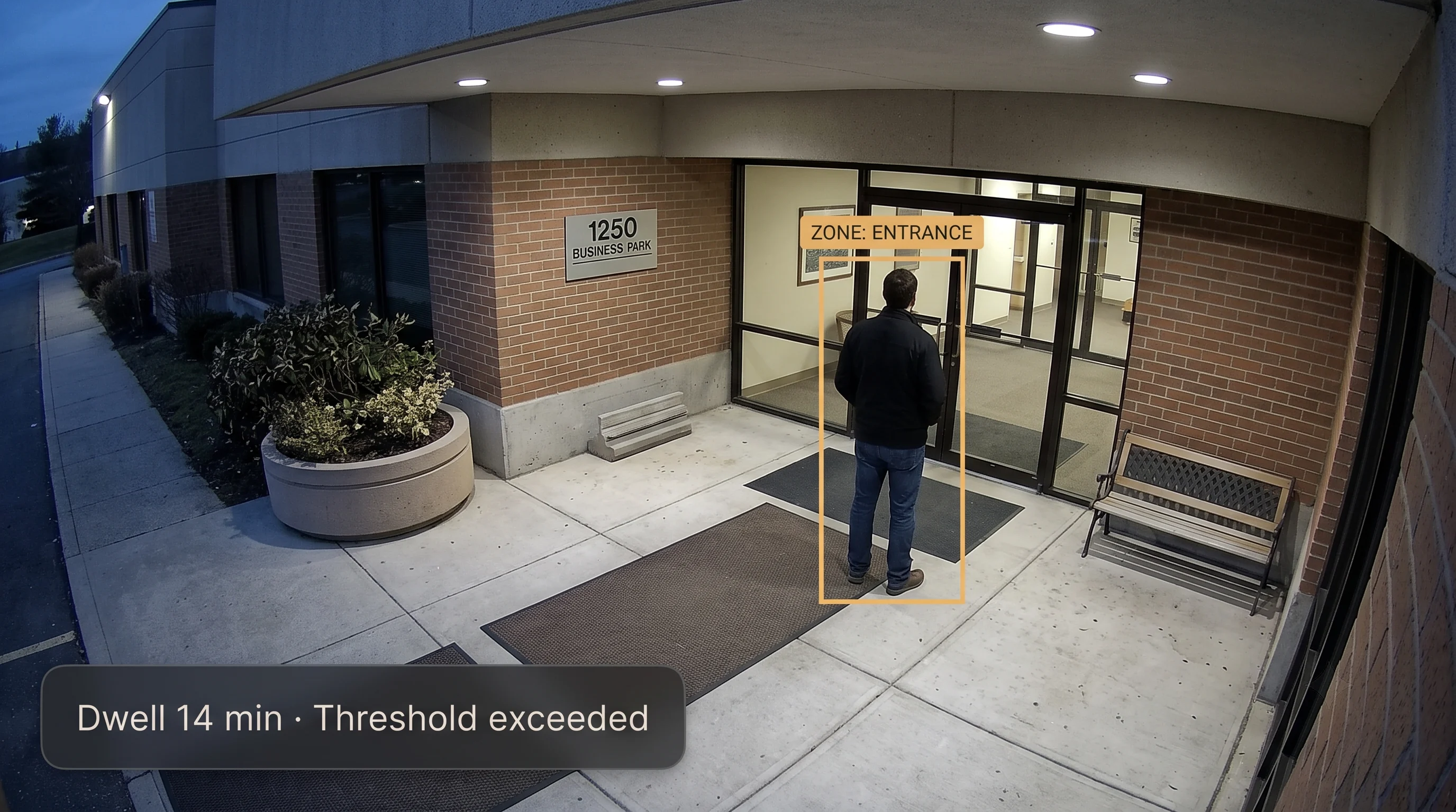AI loitering detection flagging a person who has remained in a defined zone at a building entrance longer than the configured dwell-time threshold